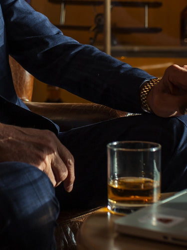 Man in a suit sitting at a bar with a glass of whiskey and a laptop.
