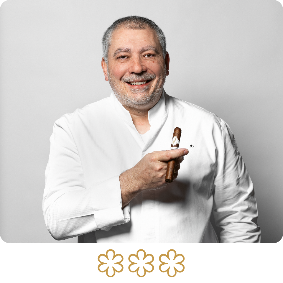 Man in a white coat holding a cigar with a gray background