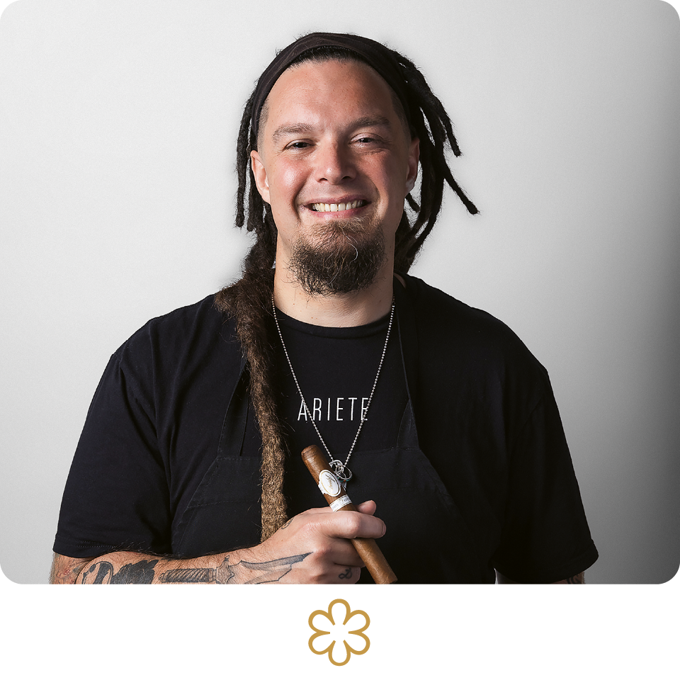 Man with dreadlocks holding a wooden object against a plain background