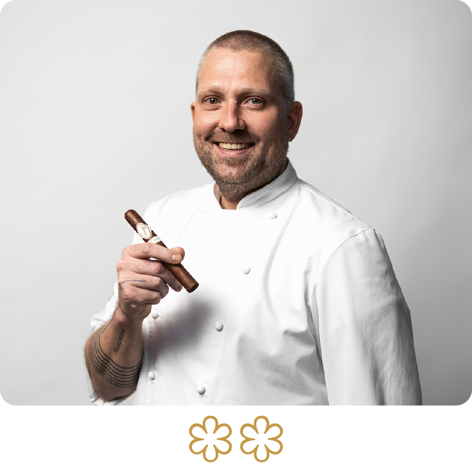 Man in a white chef's coat holding a chocolate bar against a light gray background