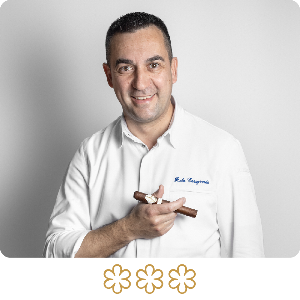 Man holding a cigar with a white shirt and 'Bodegas' text, on a gray background