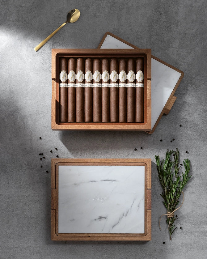 Cigar box with cigars on a gray surface with a gold spoon and greenery.