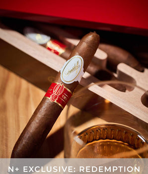 Cigar with a red band and gold label on a wooden stand with a glass of whiskey.