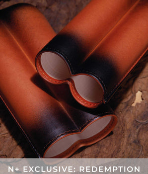 Brown leather binocular case on a wooden surface with 'N+ Exclusive: Redemption' text.