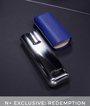 Black and blue S.T. Dupont lighter on a dark textured surface with 'N+ Exclusive: Redemption' text.