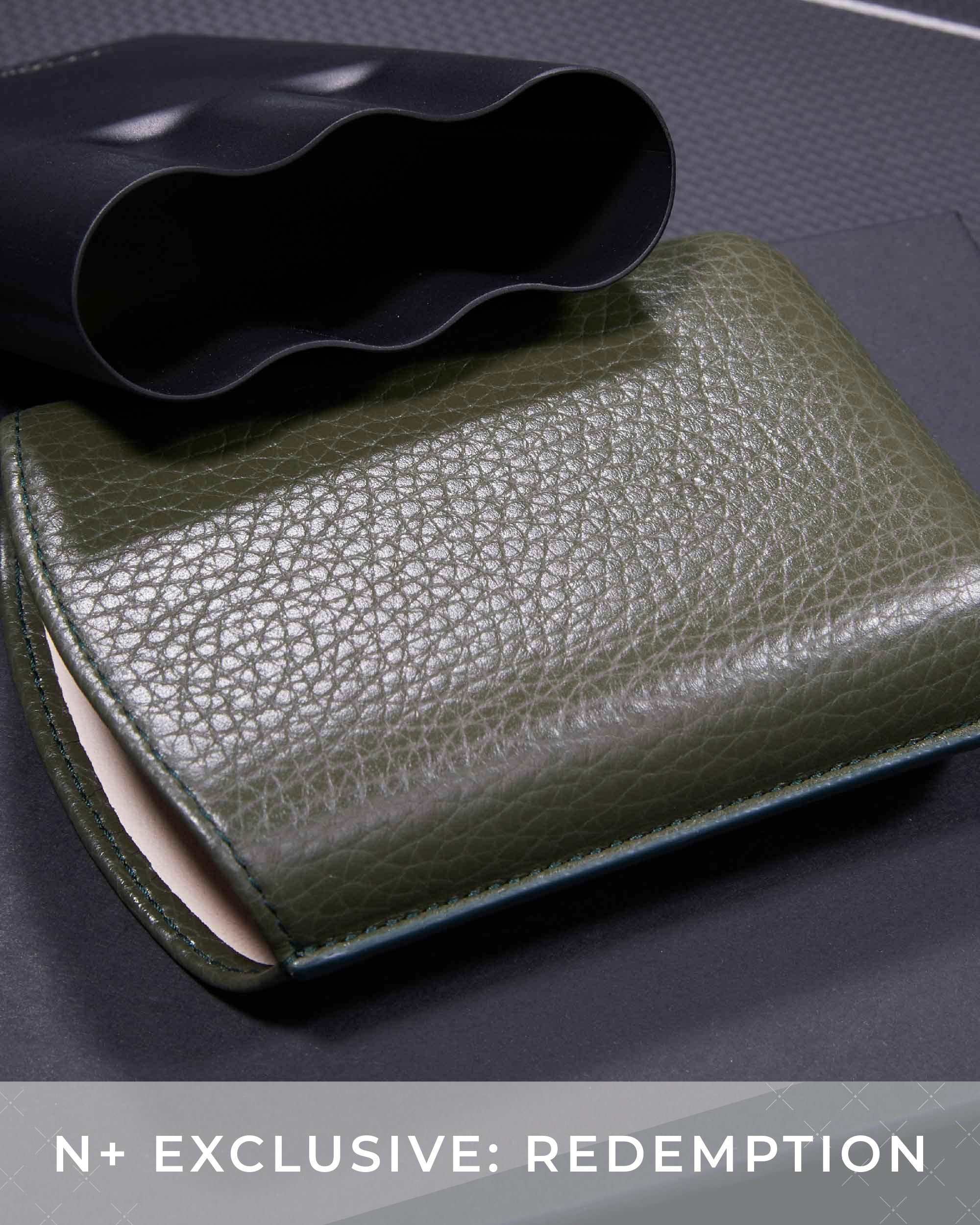 Green leather wallet on a textured surface with 'N+ Exclusive: Redemption' text.