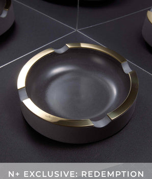 Black ashtray with gold rim on a dark surface, featuring 'N+ Exclusive: Redemption' text.