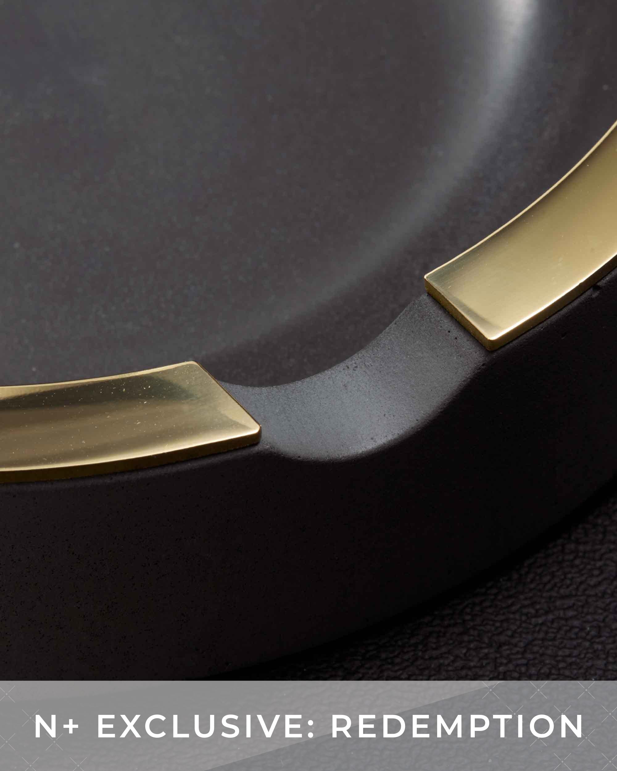 Close-up of a black frying pan with gold handles on a dark background.