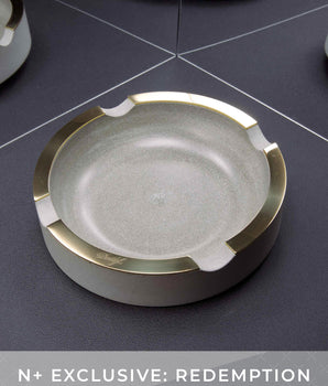 Round ashtray with gold rim on a dark surface, featuring the brand 'N+'.