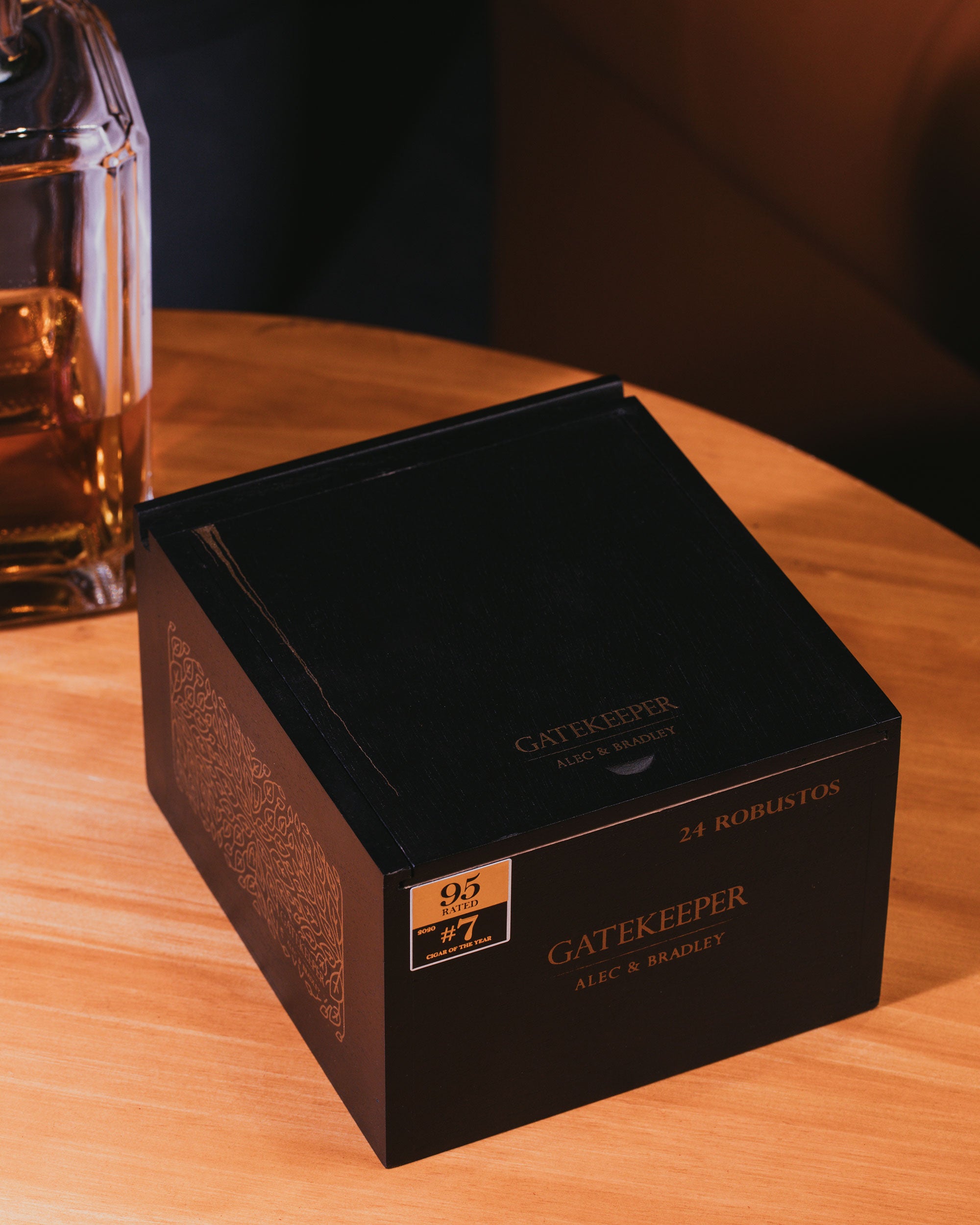 Black 'Gatekeeper' box on a wooden surface with a blurred glass of whiskey in the background.