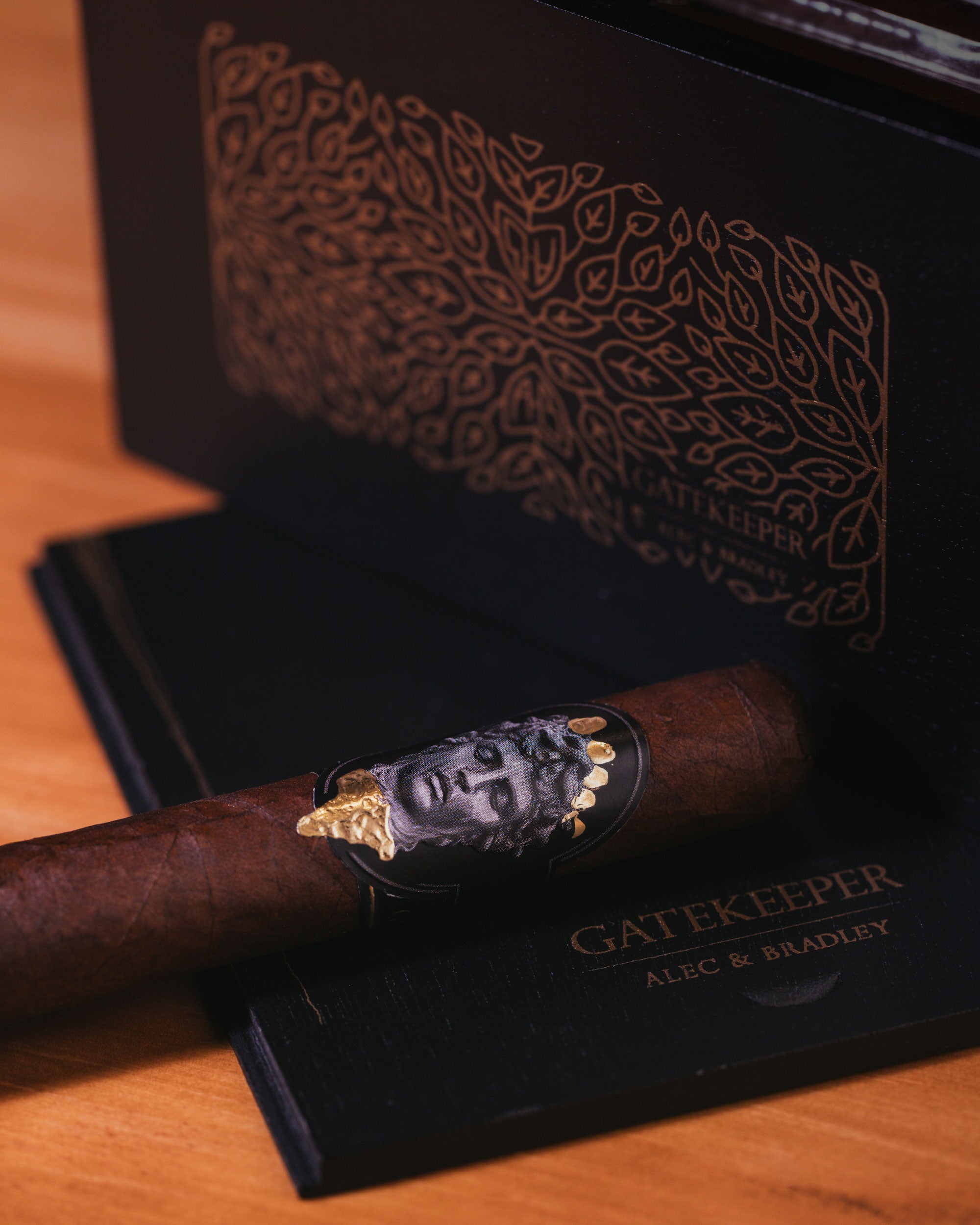 Cigar with decorative band featuring a face design on a black box labeled 'Gatekeeper' by Alec & Bradley.