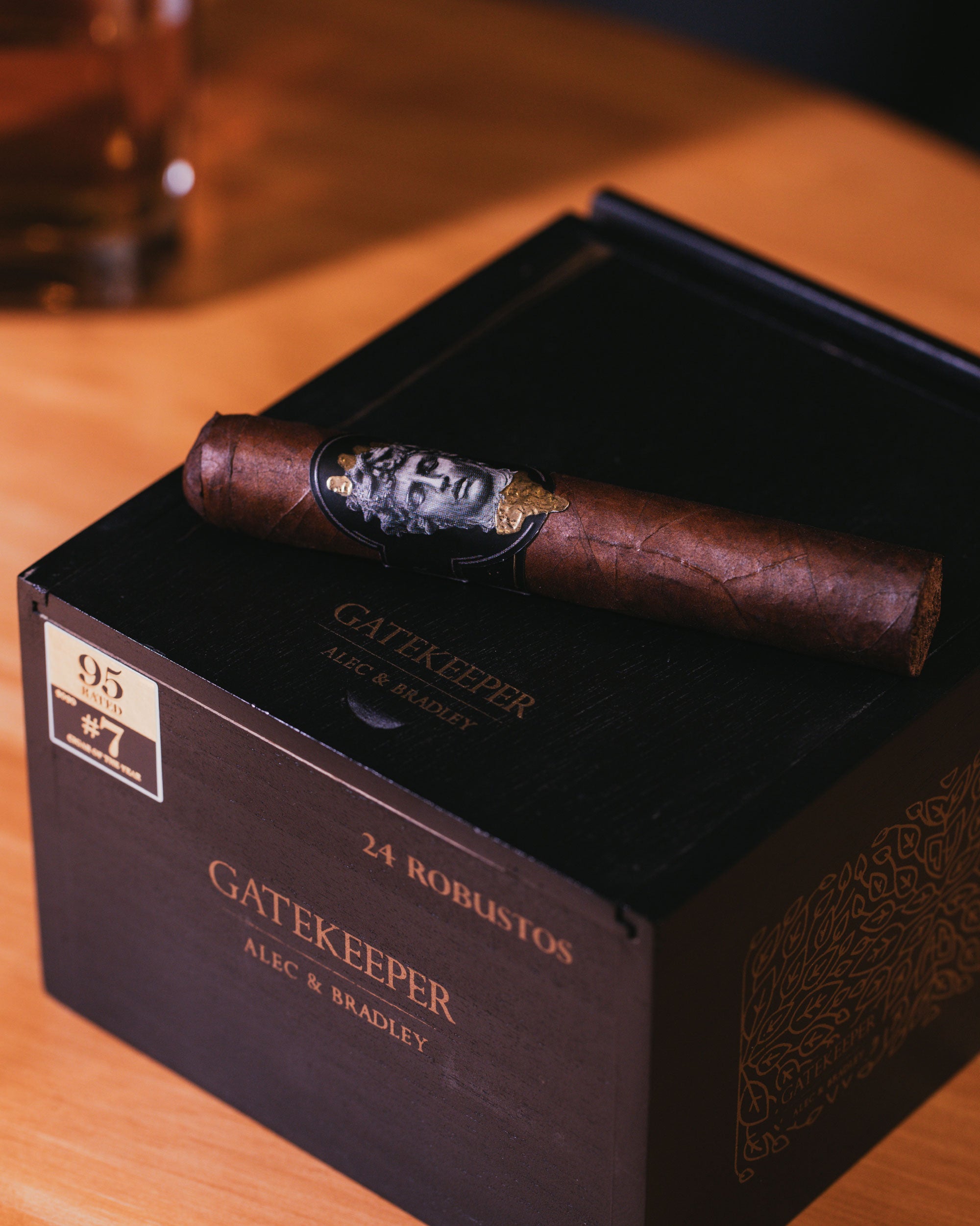 Cigar on a Gatekeeper Alec & Bradley box with a glass of whiskey in the background