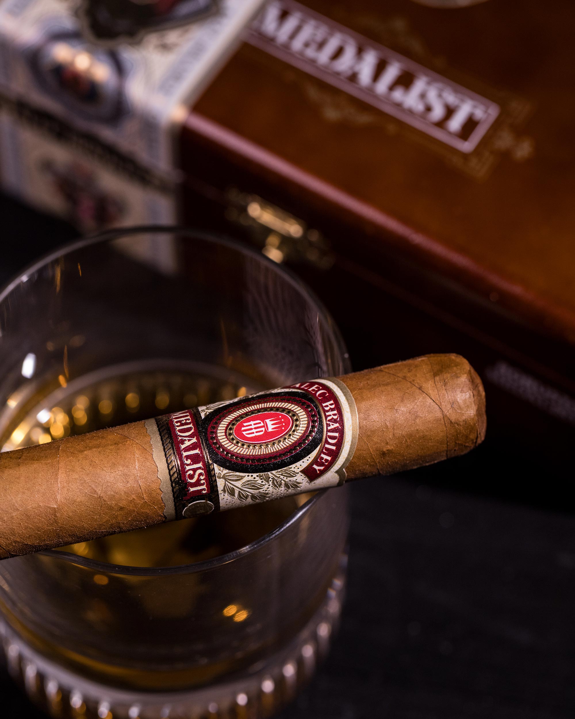 Cigar with a brand label on a reflective surface, next to a humidor.