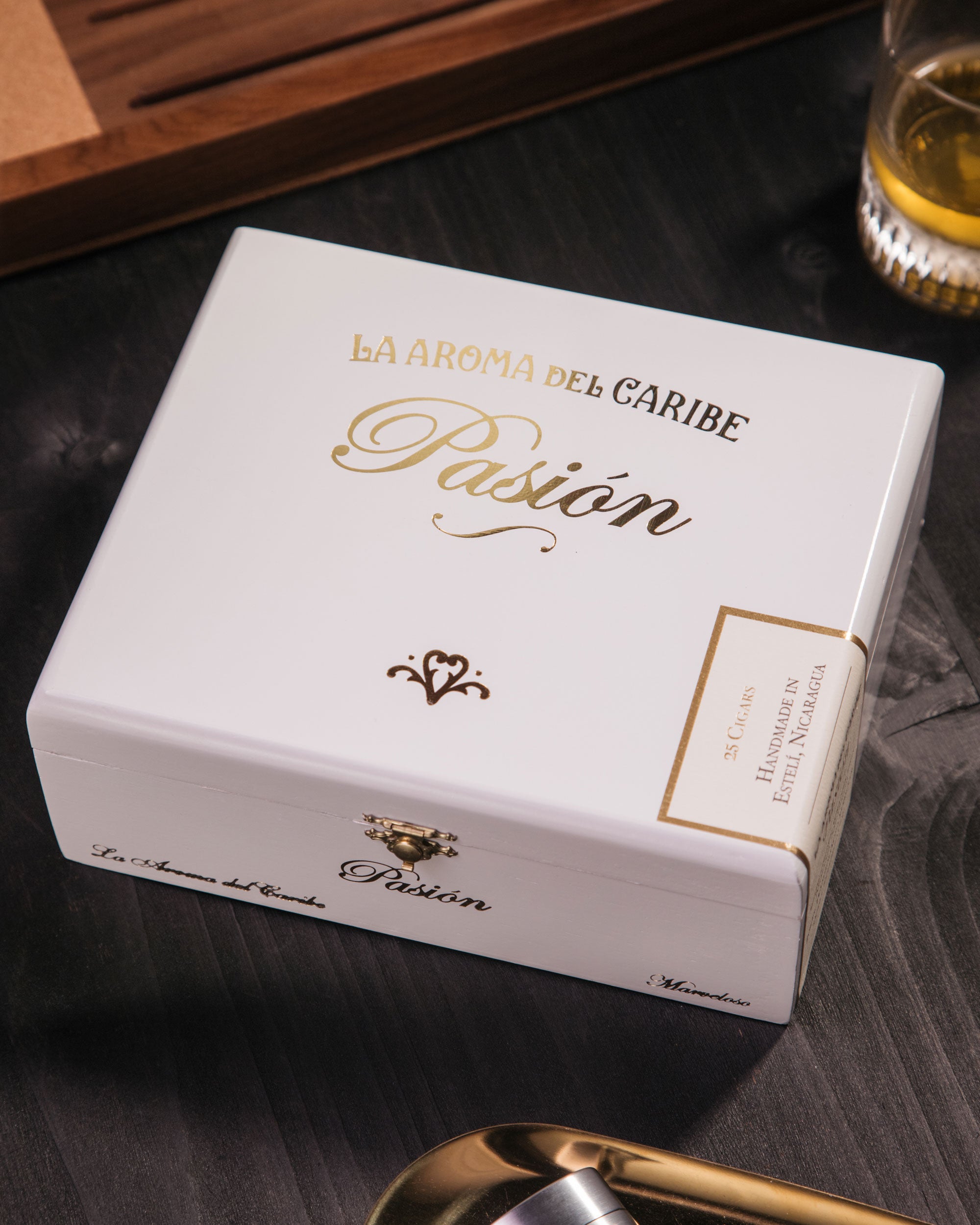 Cigar box labeled 'La Aroma del Caribe Pasion' on a dark surface with a glass of beer in the background.