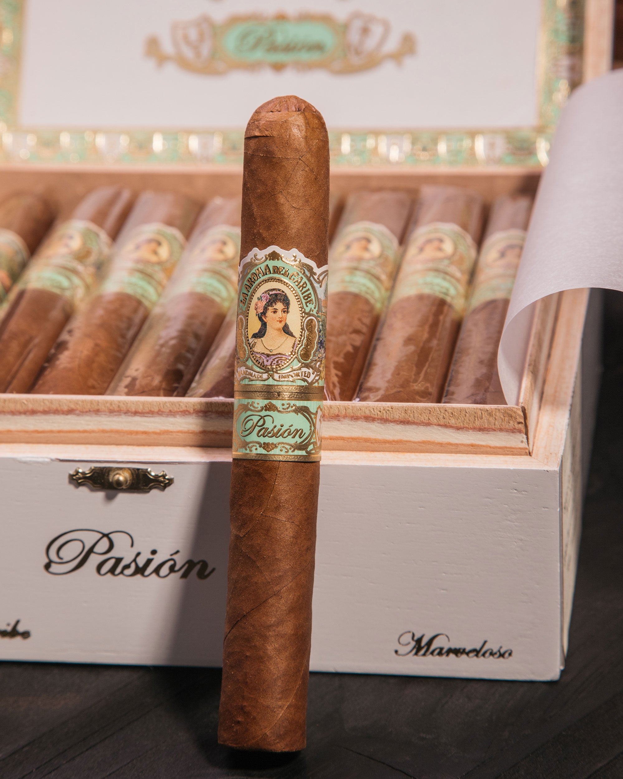 Cigar with Pasion label in front of a wooden box of cigars