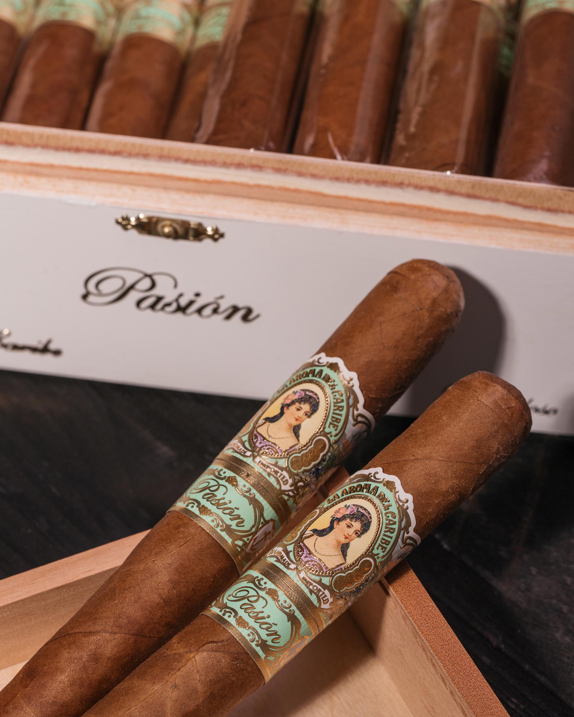 Two cigars with decorative labels on a wooden box labeled 'Pasion'.