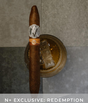 Cigar with a band on a metallic stand against a gray background, featuring 'N+ Exclusive: Redemption' text.