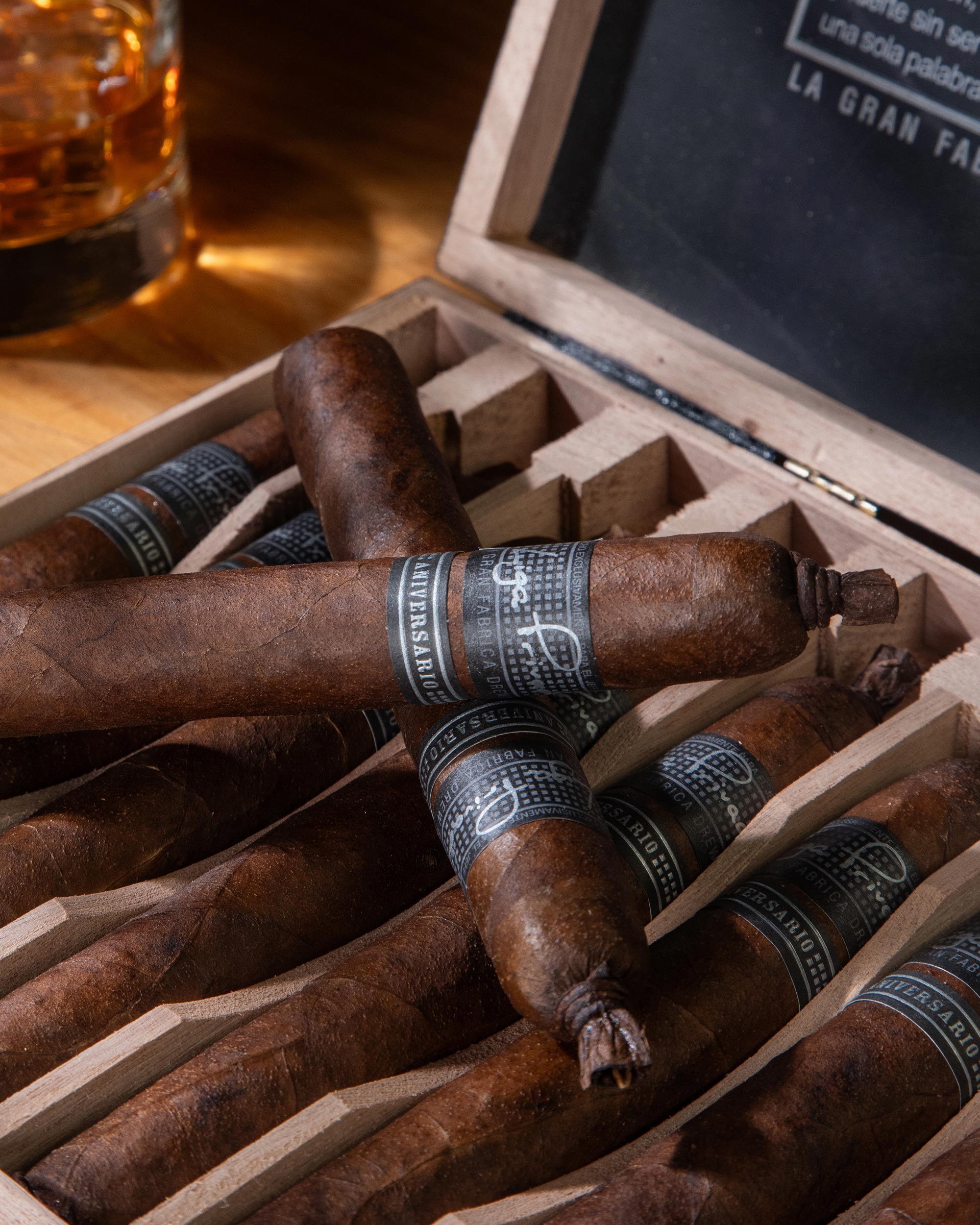Cigars in a wooden box with a glass of whiskey on a wooden table.