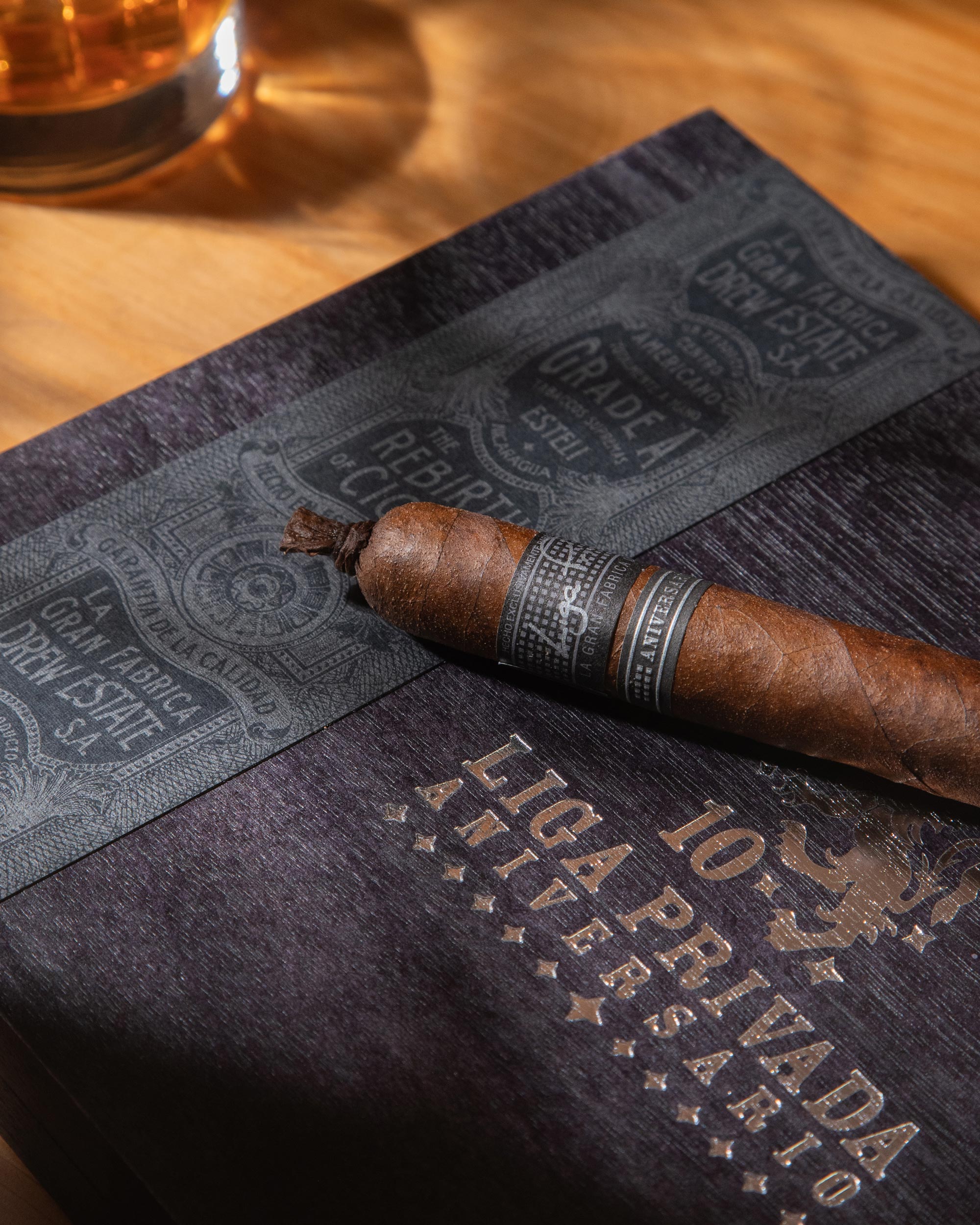Cigar on a branded humidor with a glass of whiskey in the background