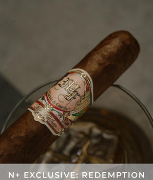 Cigar with a label on a reflective surface, featuring the text 'N+ Exclusive: Redemption'.