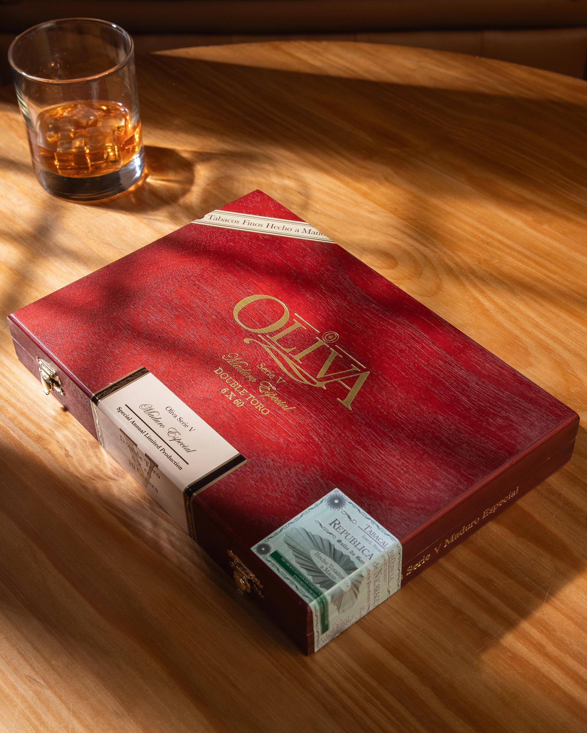 Red Oliva cigar box with a glass of whiskey on a wooden table