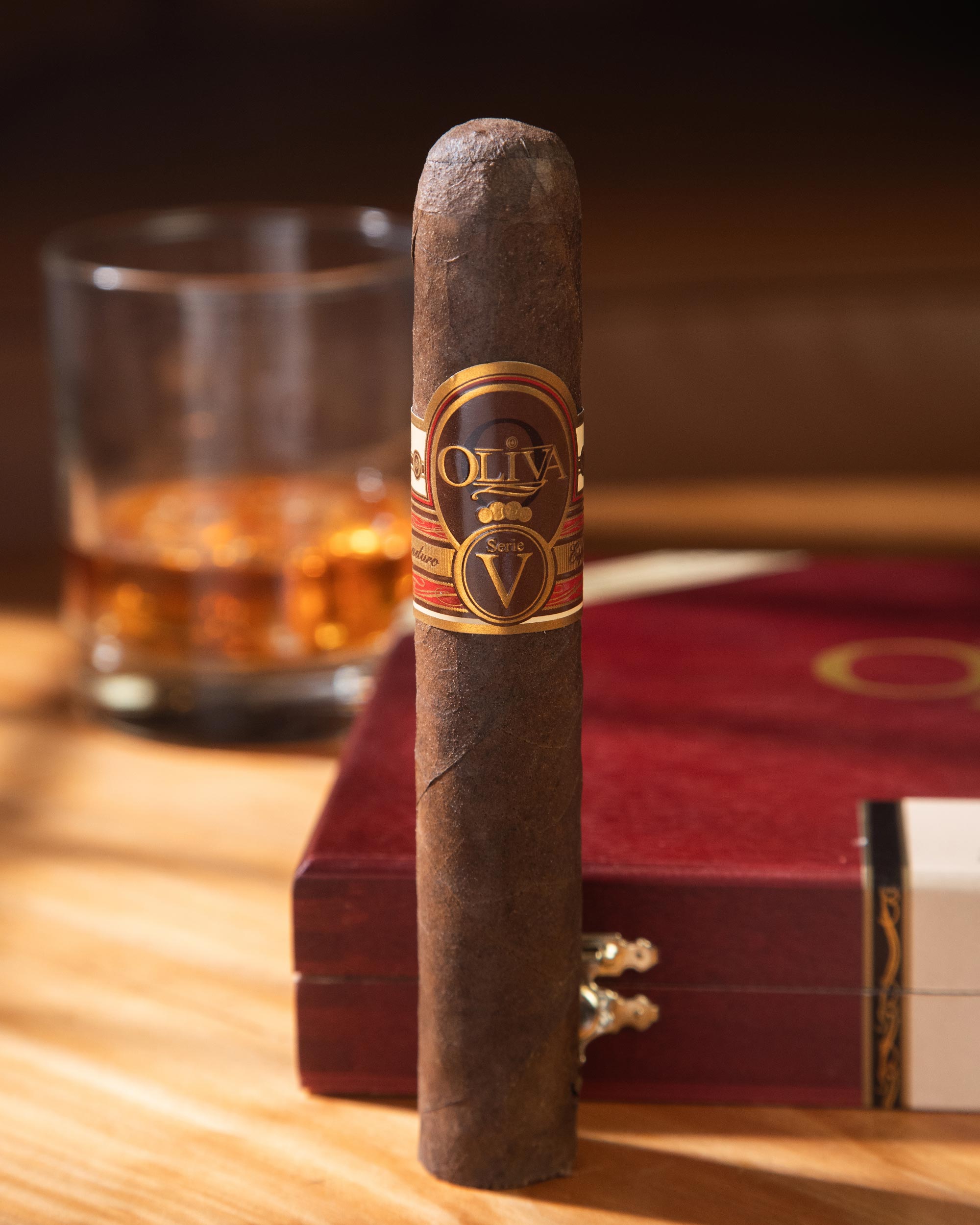 Cigar with Oliva label on a wooden table next to a glass of whiskey
