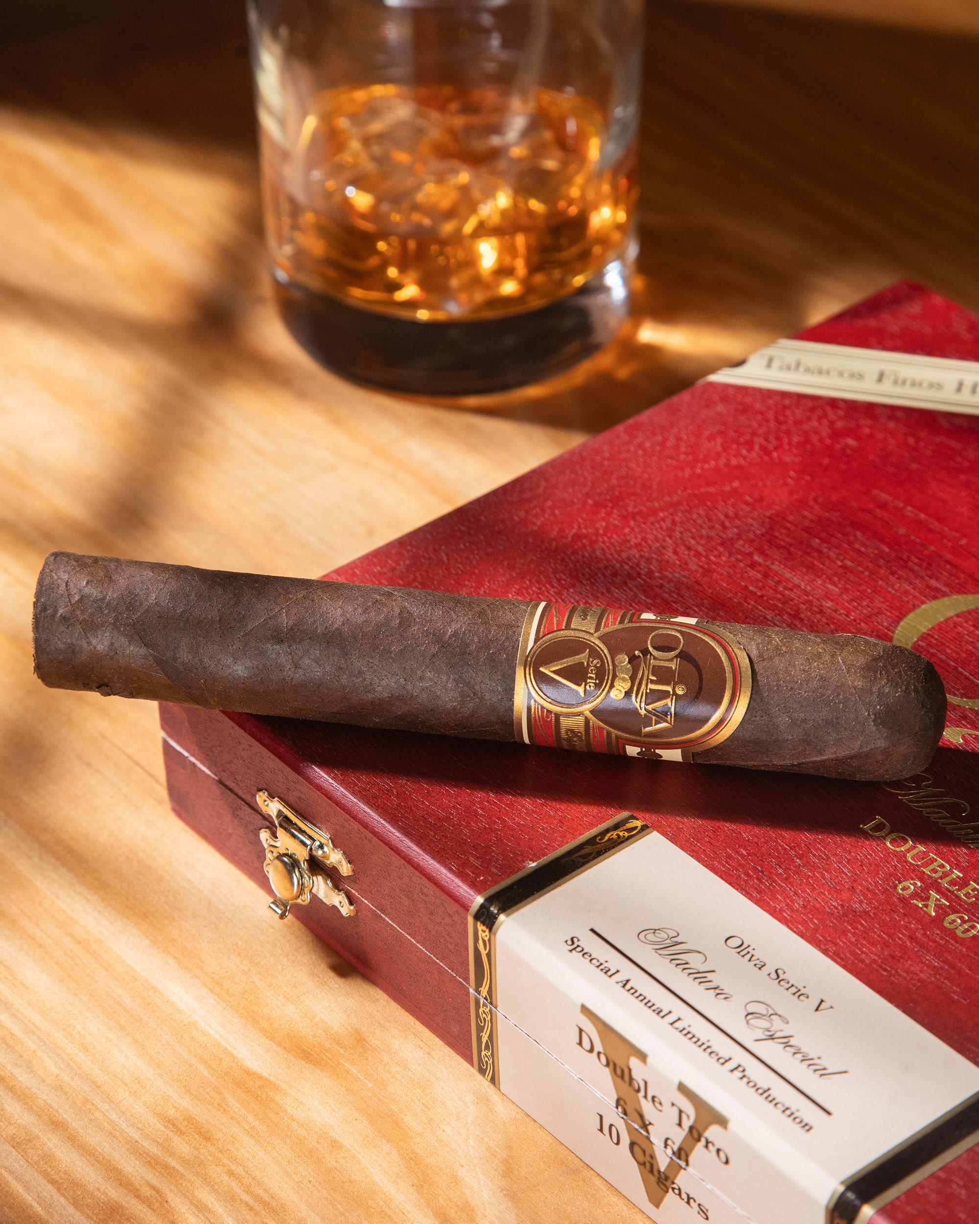 Cigar and box on a wooden table with a glass of whiskey in the background