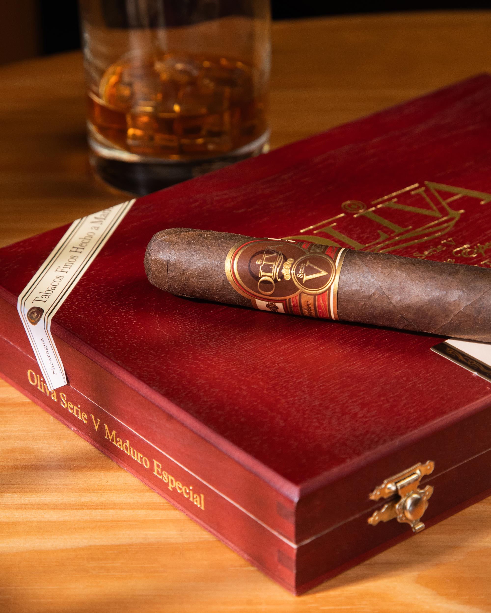 Cigar and red humidor on a wooden table with a glass of whiskey in the background