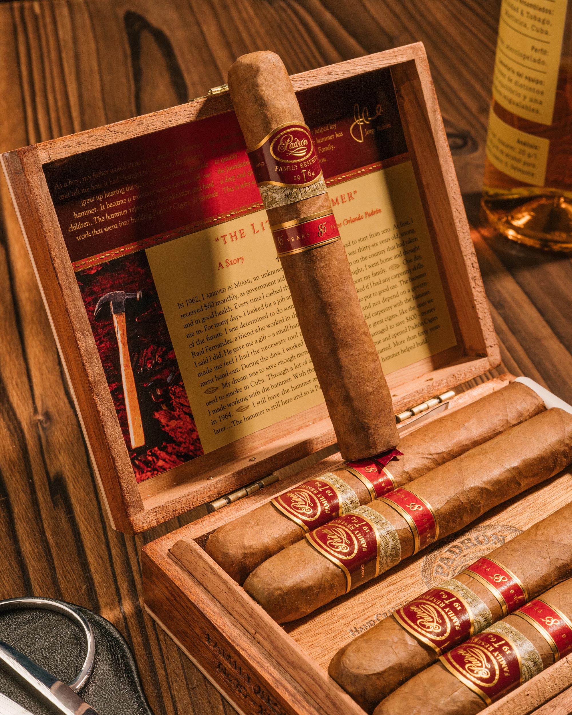 Open wooden humidor with cigars and a bottle of whiskey on a wooden surface