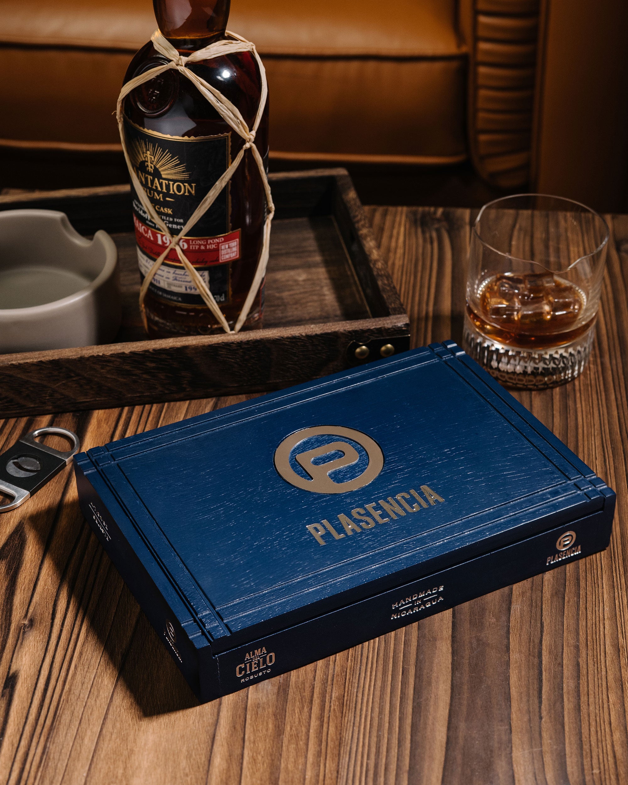 Blue Plasencia whiskey box on a wooden table with a bottle and glass in the background.