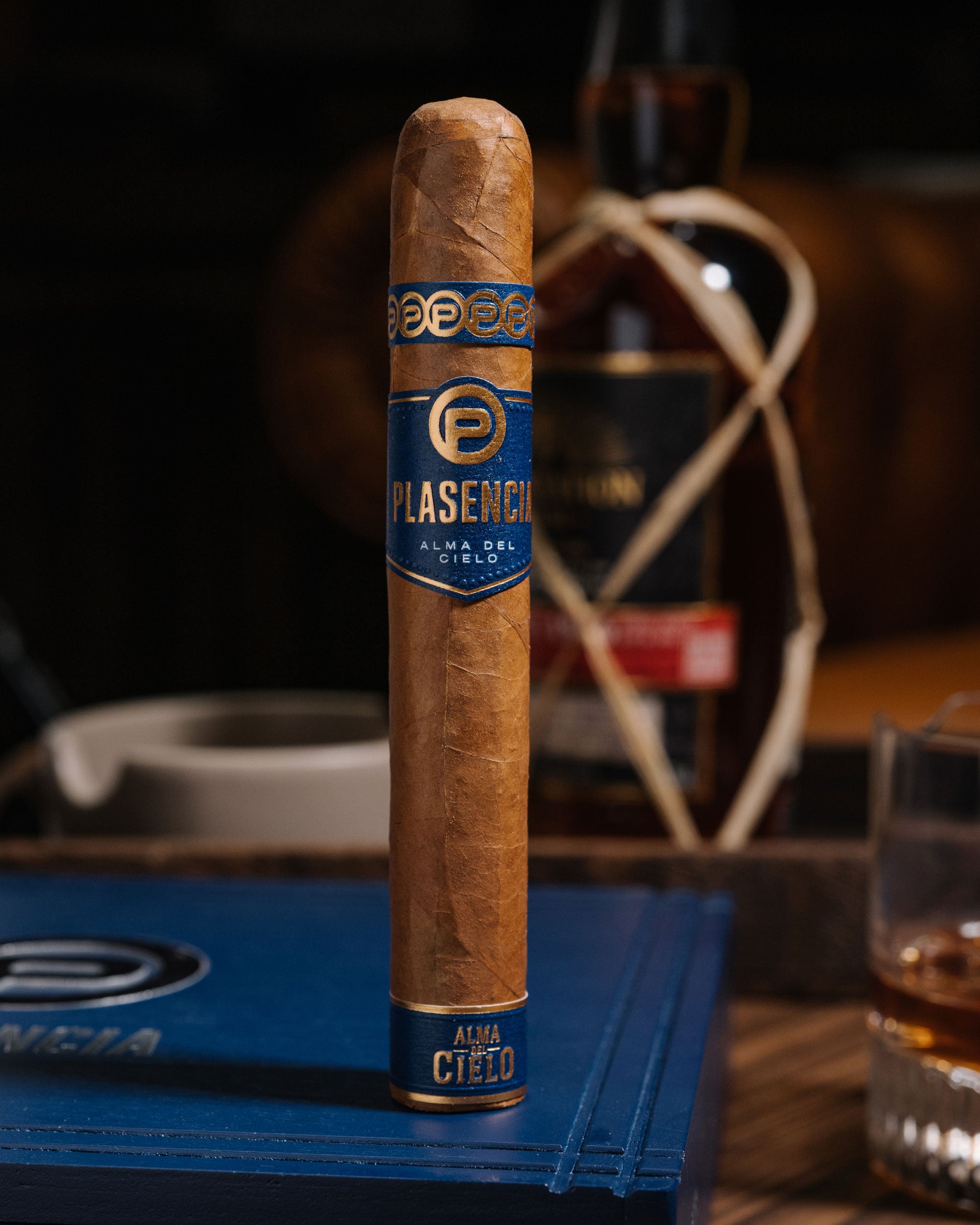 Cigar with Plasencia label on a wooden table with a bottle in the background