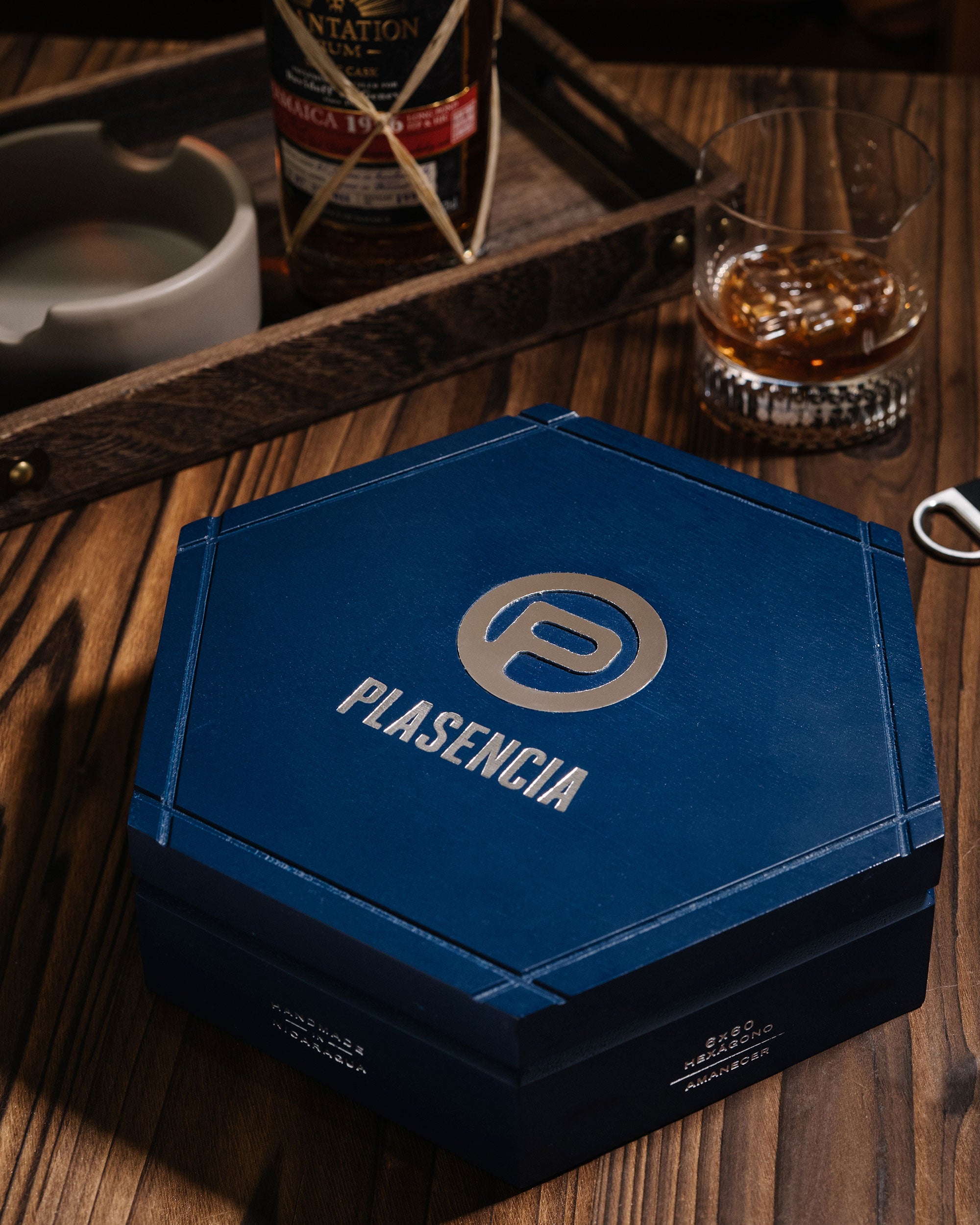 Blue Plasencia box on a wooden surface with a glass of whiskey and other items.