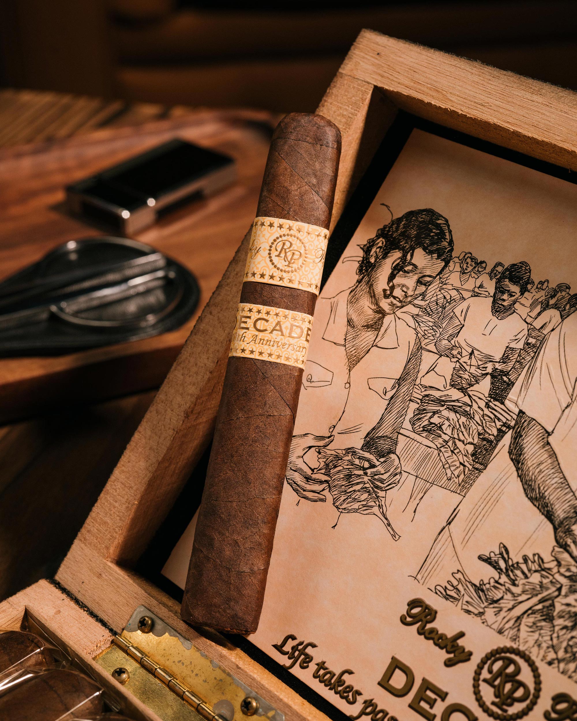 Cigar with a branded wrapper on a wooden box with illustrations, set on a wooden table.