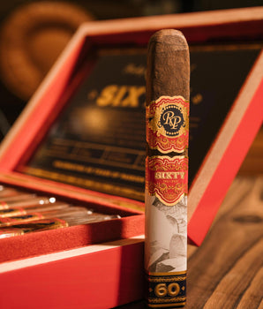 Cigar with a red and gold label in front of an open red humidor.
