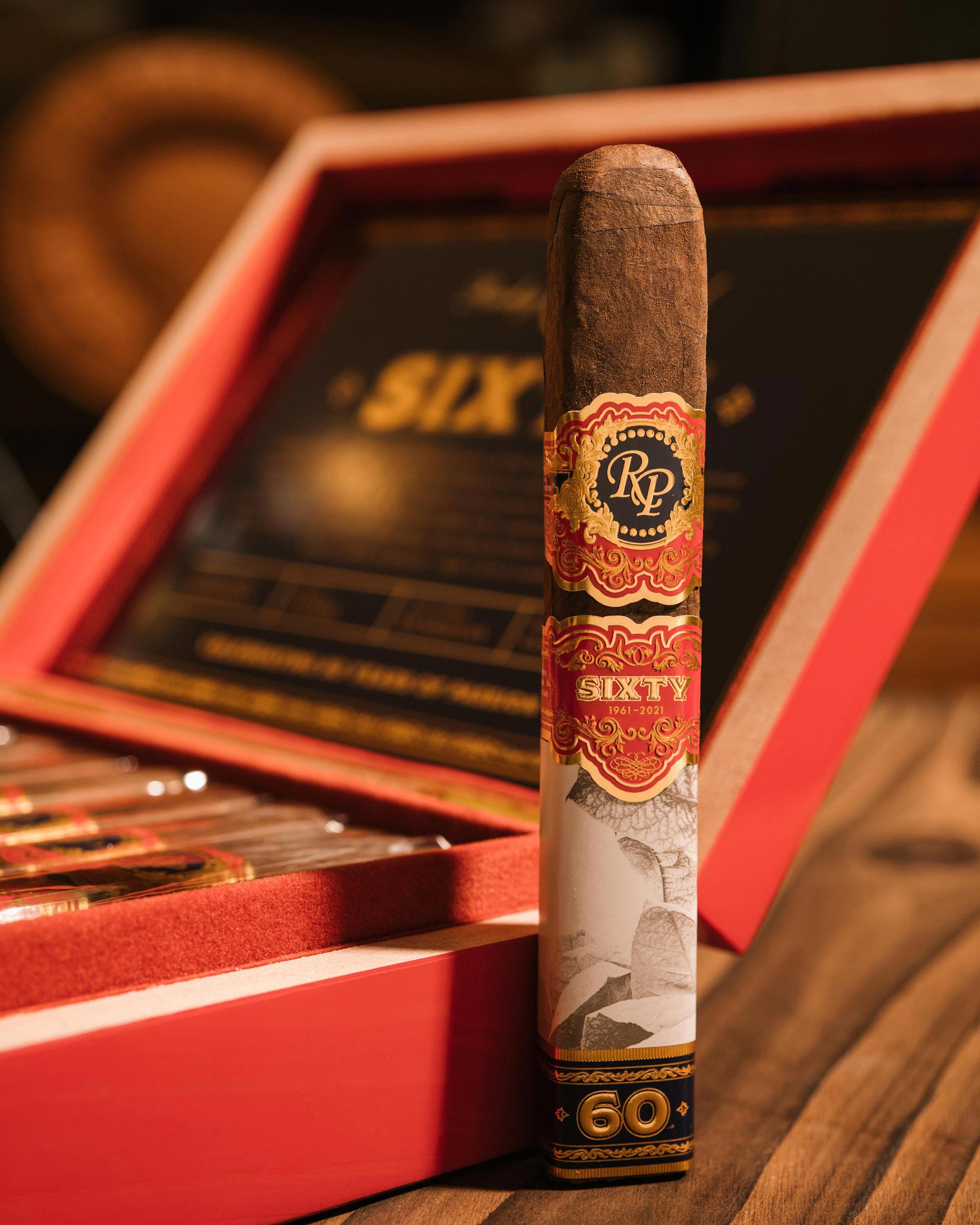 Cigar with a red and gold label in front of an open red humidor.