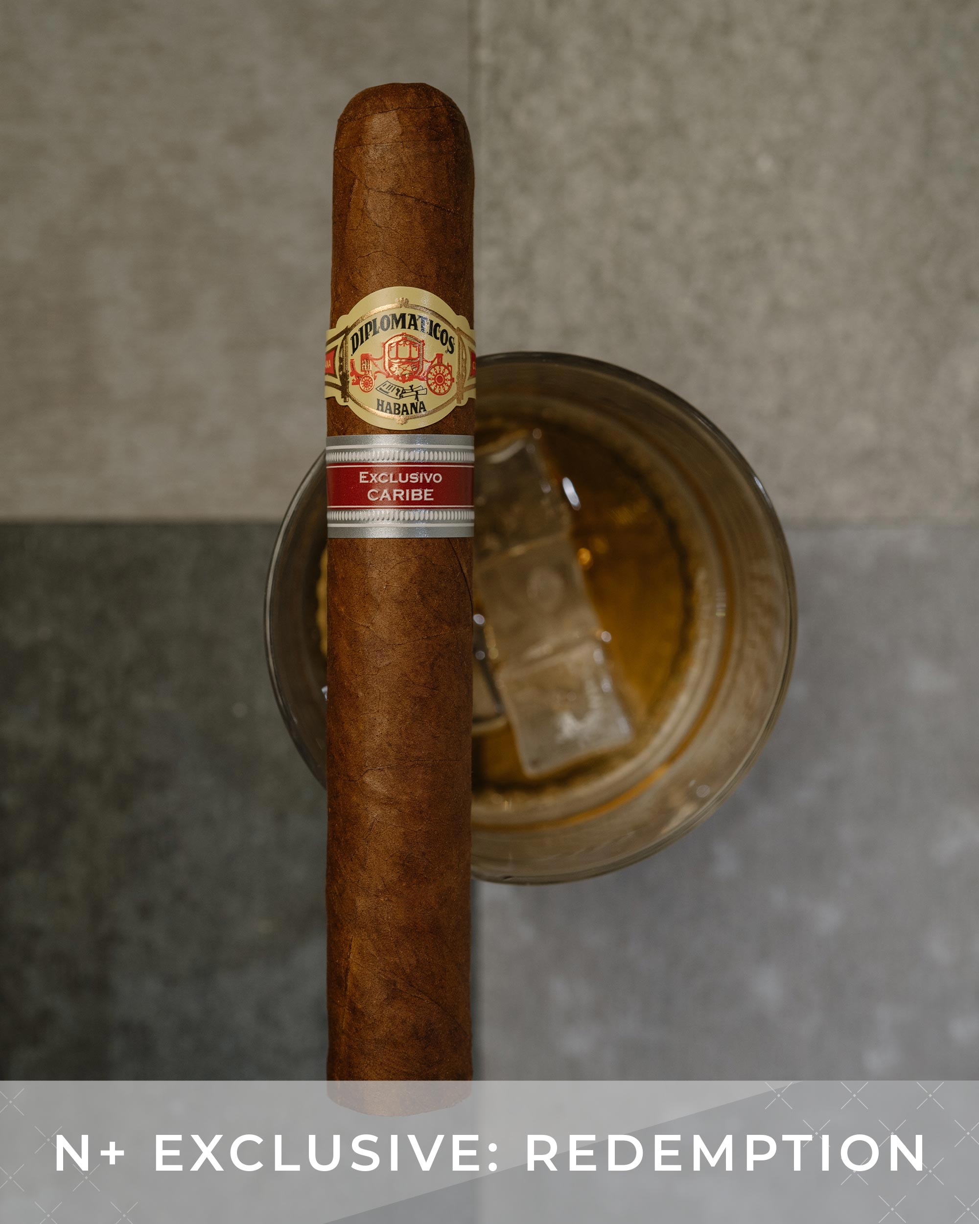 Cigar with a label on top of a glass of whiskey, against a neutral background.