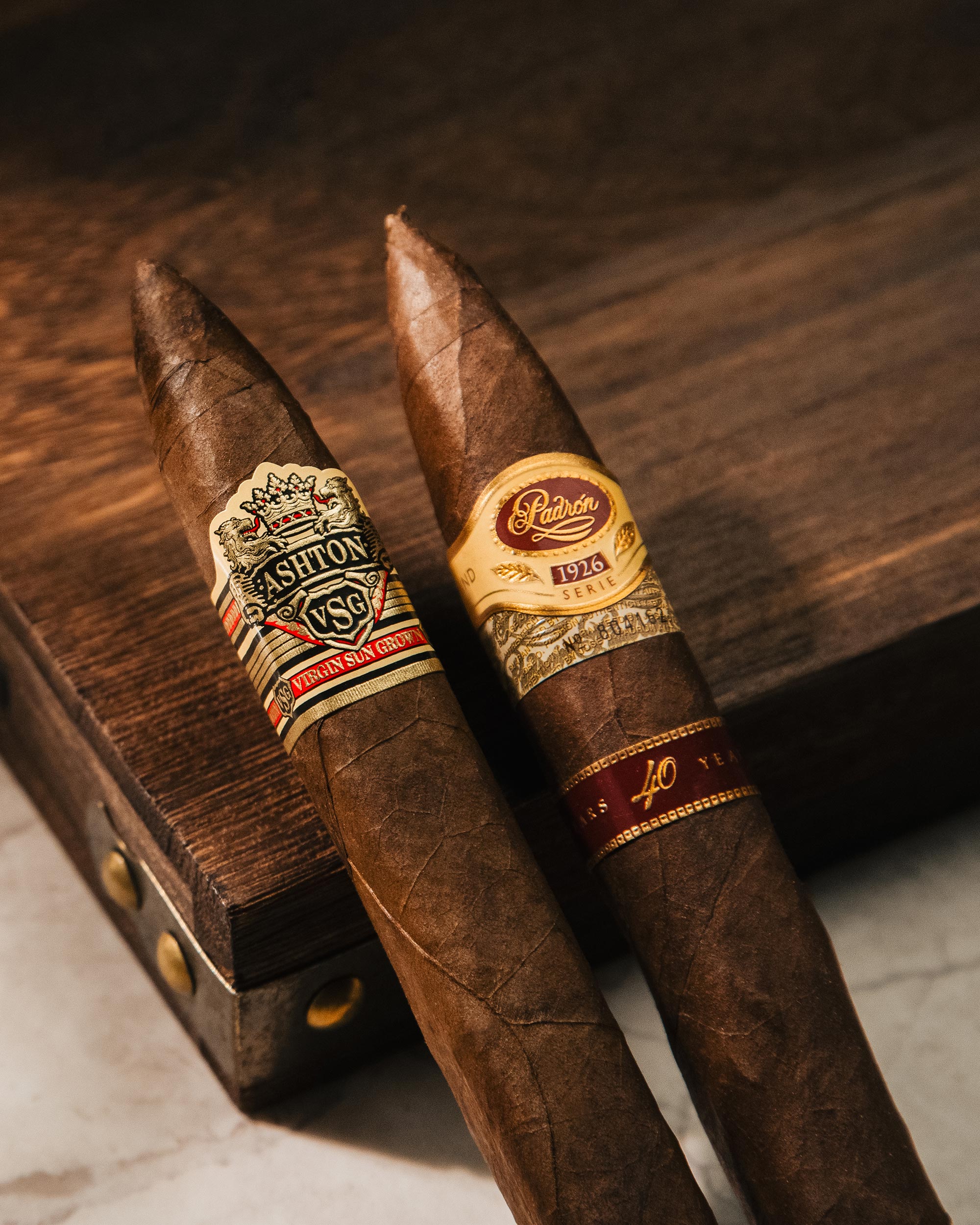 Two cigars with Ashton and Romeo y Julieta branding on a wooden surface.