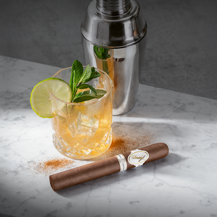 Cocktail with lime and mint, cigar, and shaker on a marble surface