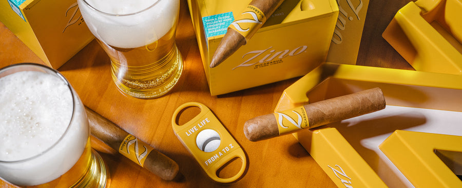 Two glasses of beer, a Zino cigar, and a Zino cigar cutter on a wooden surface.