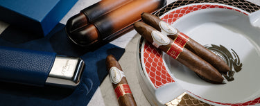Cigars on a decorative ashtray with a blue humidor in the background