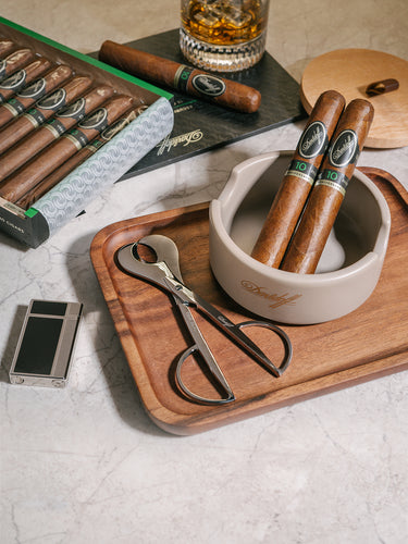 Cigars with accessories on a wooden tray, including a glass of whiskey.