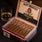 Alec Bradley Medallist cigars in an open humidor with a glass of whiskey on a dark surface.