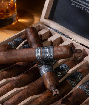 Cigars in a wooden box with a glass of whiskey on a wooden table.