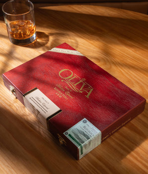 Red Oliva cigar box with a glass of whiskey on a wooden table