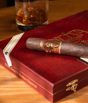 Cigar and red humidor on a wooden table with a glass of whiskey in the background