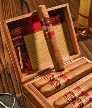 Open wooden humidor with cigars and a bottle of whiskey on a wooden surface