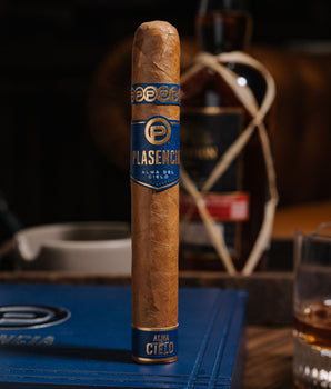 Cigar with Plasencia label on a wooden table with a bottle in the background