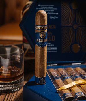 Cigar with blue wrapper on a wooden table next to a glass of whiskey