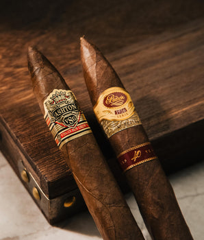 Two cigars with Ashton and Romeo y Julieta branding on a wooden surface.